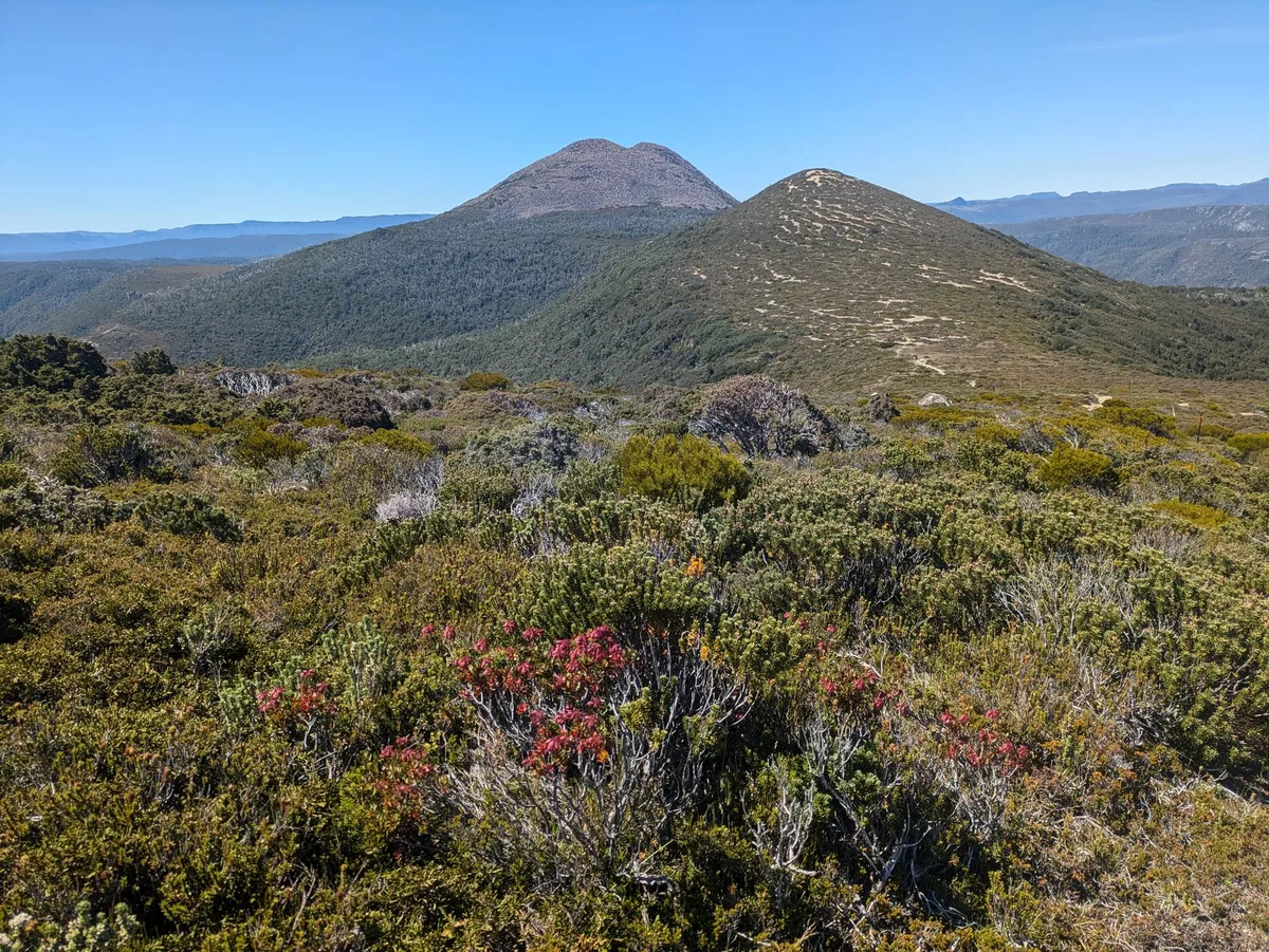 Une première colline avec des bouts de sente visibles et une montagne de pierriers derrière elle